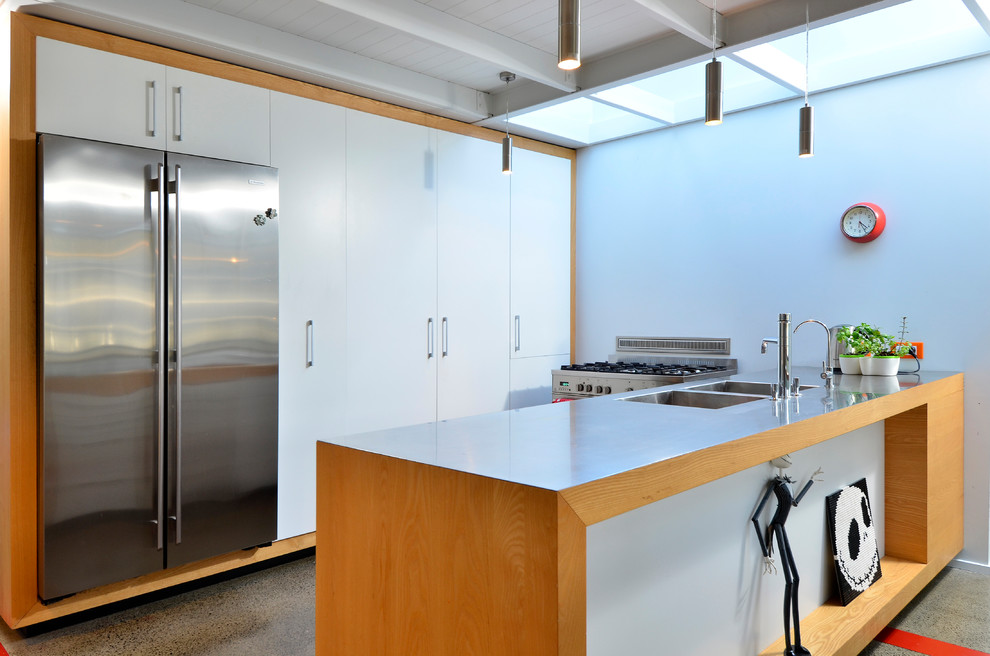 Design ideas for a midcentury galley kitchen in Auckland with an integrated sink, flat-panel cabinets, white cabinets, stainless steel benchtops, stainless steel appliances, concrete floors, a peninsula and grey floor.