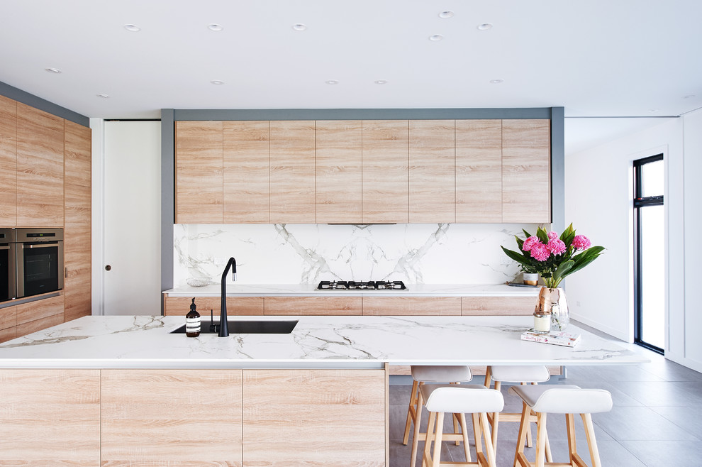 Design ideas for a mid-sized contemporary l-shaped kitchen in Melbourne with flat-panel cabinets, light wood cabinets, white splashback, marble splashback, black appliances, with island, grey floor and white benchtop.