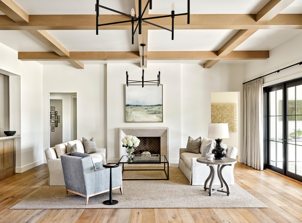 This is an example of a large transitional formal open concept living room in Phoenix with white walls, light hardwood floors, a standard fireplace, a plaster fireplace surround, no tv, beige floor and coffered.