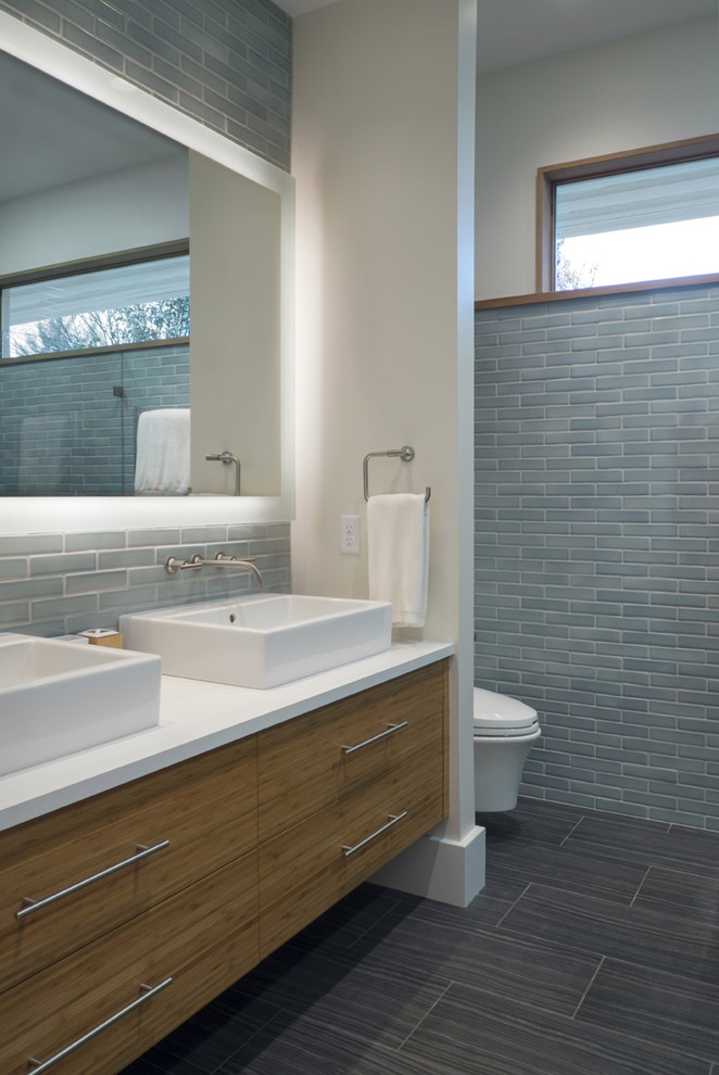 Photo of a mid-sized modern master bathroom in Louisville with flat-panel cabinets, medium wood cabinets, a wall-mount toilet, blue tile, ceramic tile, white walls, ceramic floors, engineered quartz benchtops and a vessel sink.