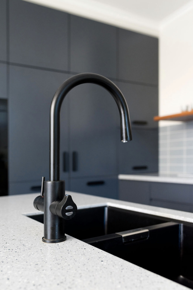 This is an example of a mid-sized contemporary l-shaped kitchen pantry in Canberra - Queanbeyan with an undermount sink, flat-panel cabinets, blue cabinets, terrazzo benchtops, blue splashback, subway tile splashback, black appliances, laminate floors, with island, beige floor, blue benchtop and vaulted.