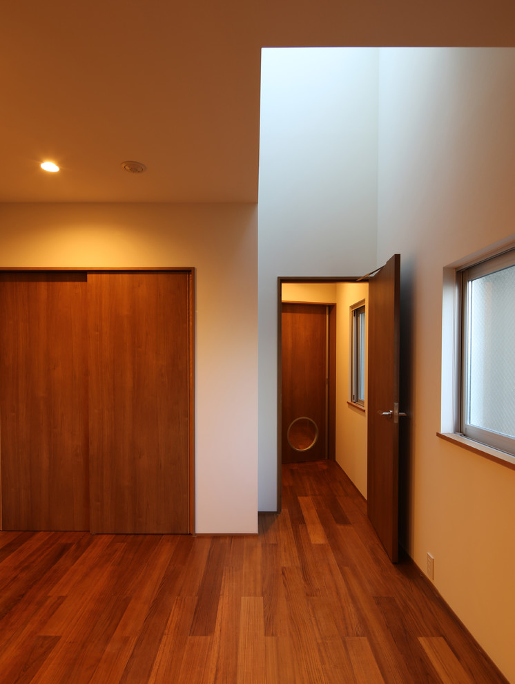 Imagen de dormitorio principal moderno de tamaño medio sin chimenea con paredes blancas, suelo de madera en tonos medios, marco de chimenea de yeso y suelo marrón