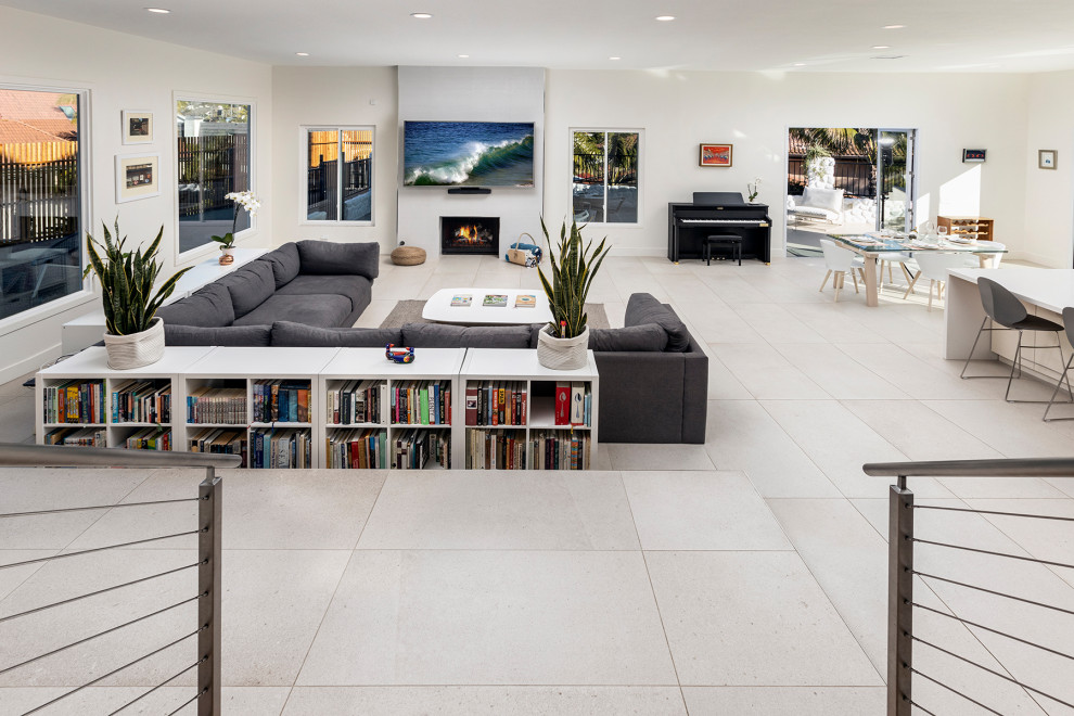 This is an example of a large contemporary open concept living room in Orange County with white walls, plywood floors, a standard fireplace, a wall-mounted tv and white floor.