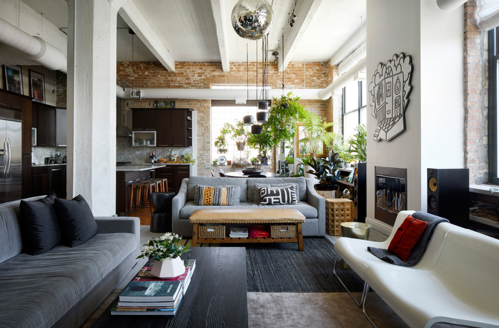 Mid-sized industrial open concept living room in Chicago with a music area, white walls, light hardwood floors, a standard fireplace, a concealed tv, exposed beam and brick walls.