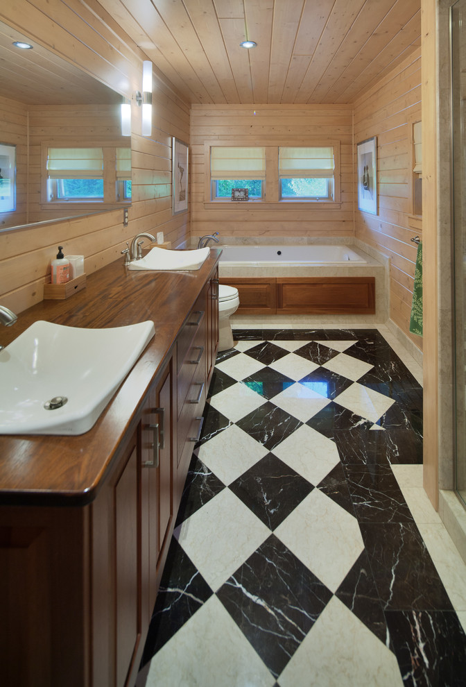 This is an example of a small country master bathroom in Detroit with a drop-in sink, raised-panel cabinets, dark wood cabinets, wood benchtops, a drop-in tub, an alcove shower, a one-piece toilet, marble floors and brown benchtops.