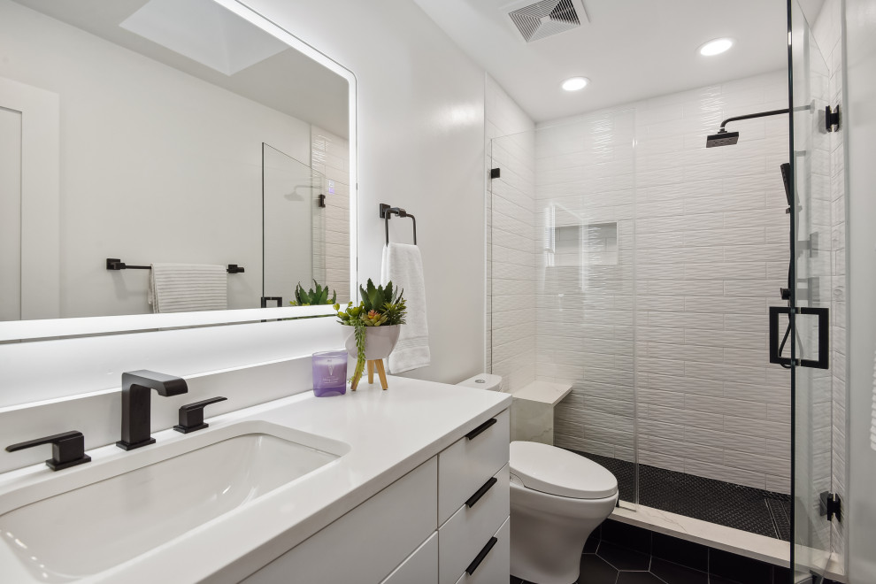 Пример оригинального дизайна: ванная комната среднего размера в стиле модернизм с плоскими фасадами, белыми фасадами, душем в нише, биде, белой плиткой, керамической плиткой, белыми стенами, полом из керамической плитки, душевой кабиной, врезной раковиной, столешницей из искусственного кварца, черным полом, душем с распашными дверями, белой столешницей, сиденьем для душа, тумбой под одну раковину и подвесной тумбой