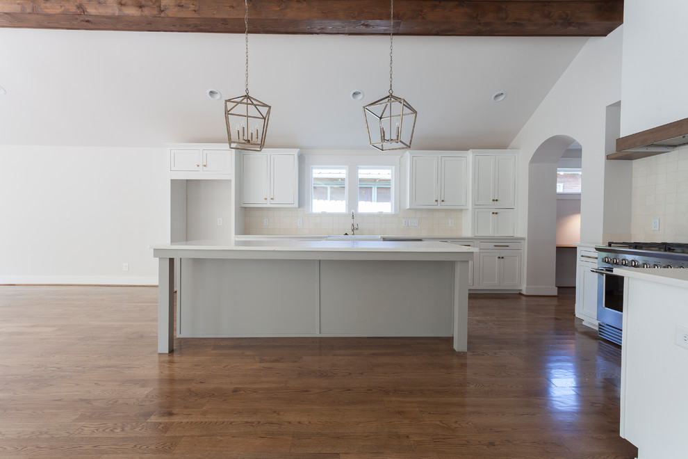 Inspiration for a mid-sized transitional l-shaped open plan kitchen in Nashville with a farmhouse sink, recessed-panel cabinets, white cabinets, quartz benchtops, stainless steel appliances, medium hardwood floors, with island, white benchtop and limestone splashback.