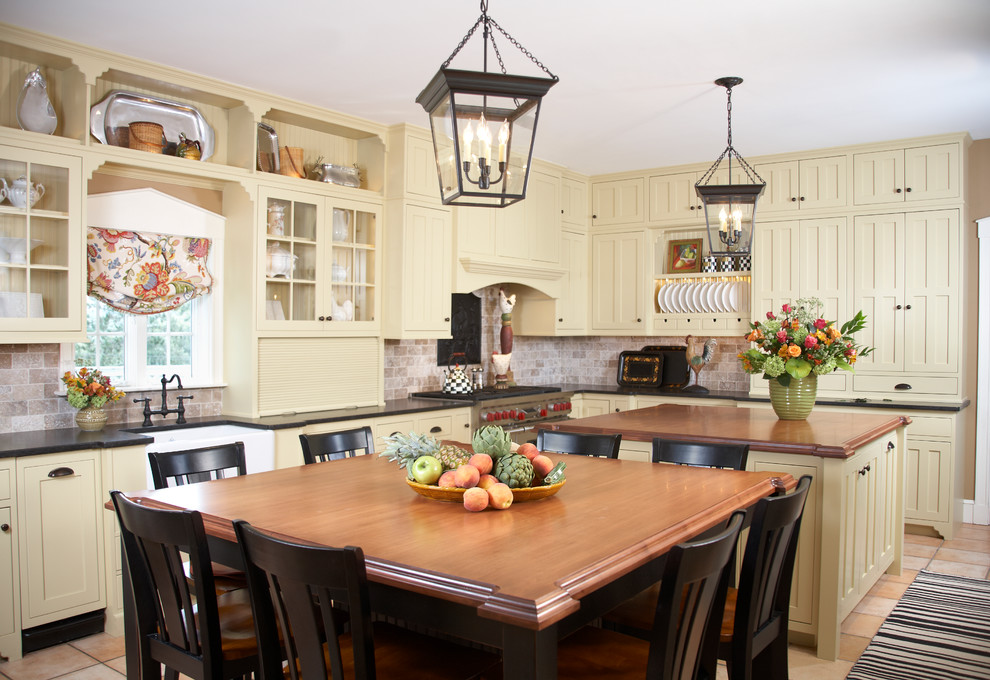 Photo of a traditional eat-in kitchen in Boston with a farmhouse sink, shaker cabinets, yellow cabinets, wood benchtops, brown splashback, stainless steel appliances and limestone splashback.