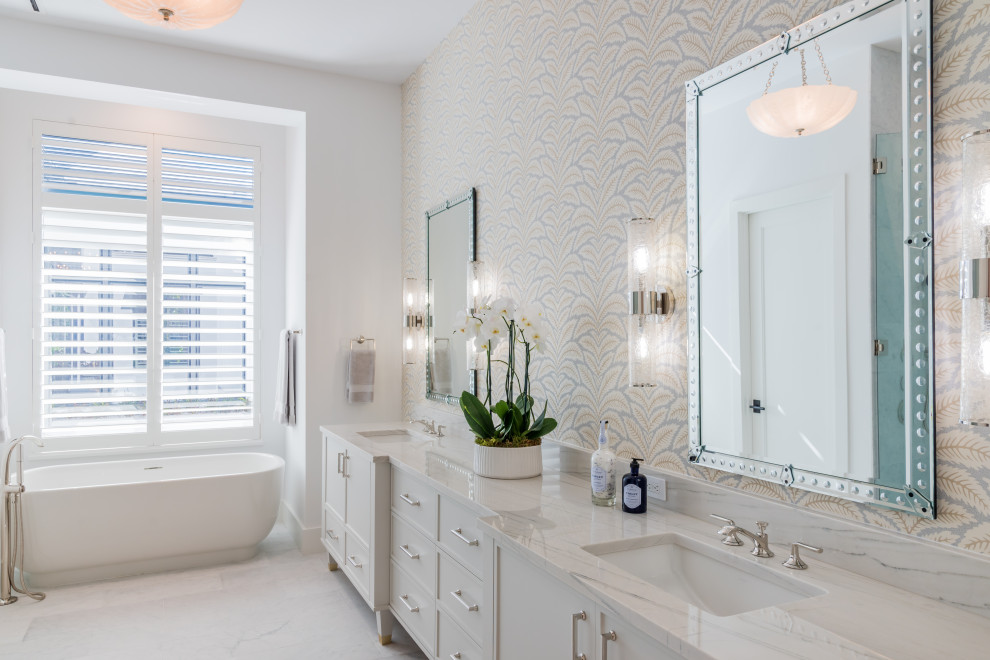This is an example of a large beach style master bathroom in Miami with shaker cabinets, white cabinets, a freestanding tub, white walls, porcelain floors, an undermount sink, white floor and white benchtops.