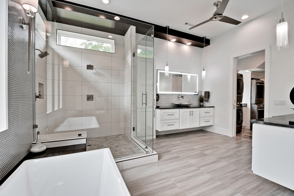 This is an example of a large modern master bathroom in Other with raised-panel cabinets, white cabinets, a freestanding tub, an open shower, a two-piece toilet, gray tile, porcelain tile, grey walls, porcelain floors, a trough sink, granite benchtops, grey floor, a hinged shower door, black benchtops, a double vanity and a floating vanity.