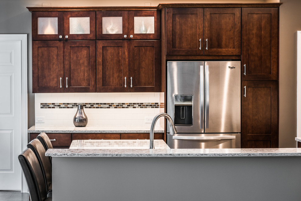 Example of a mid-sized transitional u-shaped vinyl floor and brown floor kitchen design with an undermount sink, recessed-panel cabinets, brown cabinets, quartz countertops, multicolored backsplash, porcelain backsplash, stainless steel appliances, a peninsula and multicolored countertops