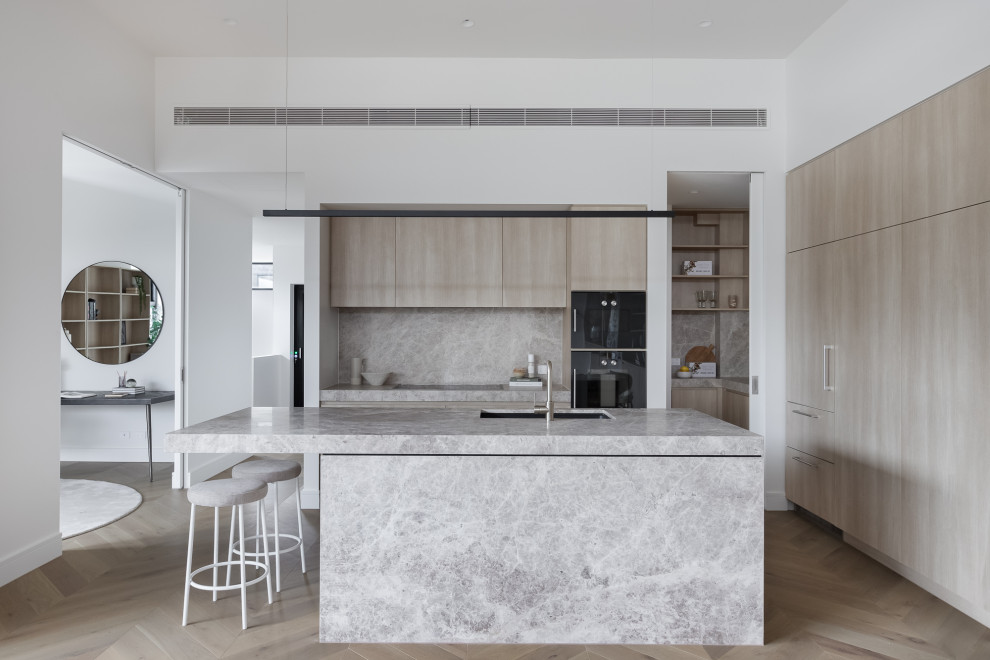 Inspiration for a modern l-shaped kitchen in Melbourne with an undermount sink, flat-panel cabinets, light wood cabinets, black appliances, light hardwood floors, with island, beige floor and grey benchtop.