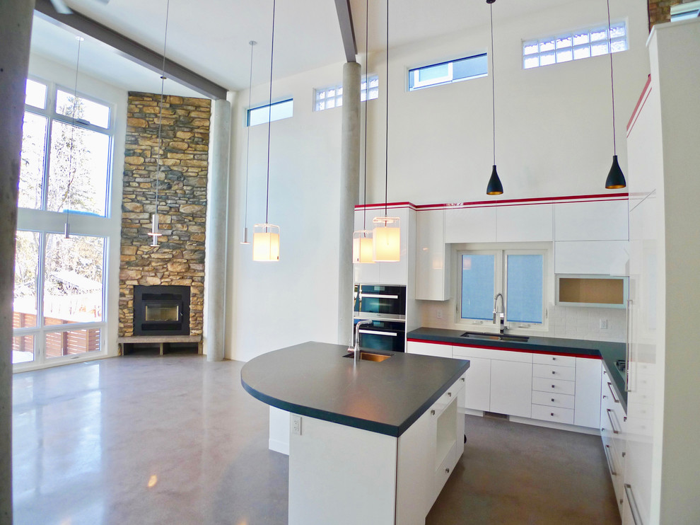 Open concept kitchen - contemporary l-shaped concrete floor and gray floor open concept kitchen idea in Edmonton with an undermount sink, flat-panel cabinets, white cabinets, quartz countertops, white backsplash, glass tile backsplash, stainless steel appliances, an island and black countertops