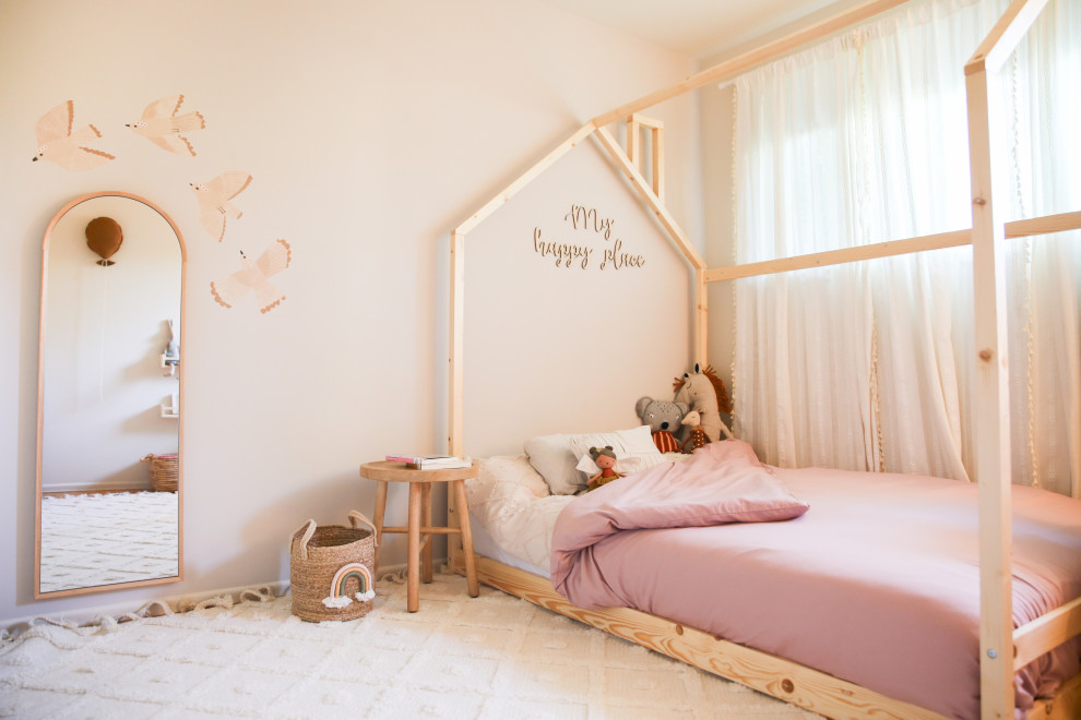 This is an example of a medium sized scandinavian toddler’s room for girls in San Francisco with beige walls and light hardwood flooring.