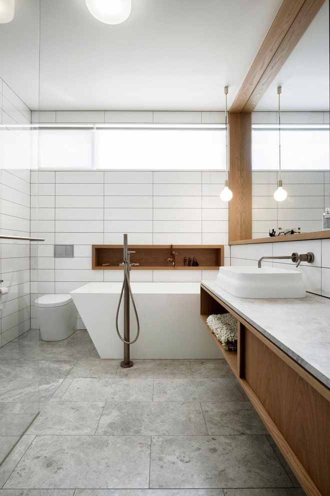 Design ideas for a midcentury bathroom in Melbourne with a freestanding tub, white tile, marble benchtops, flat-panel cabinets, medium wood cabinets, a vessel sink, grey floor and white benchtops.