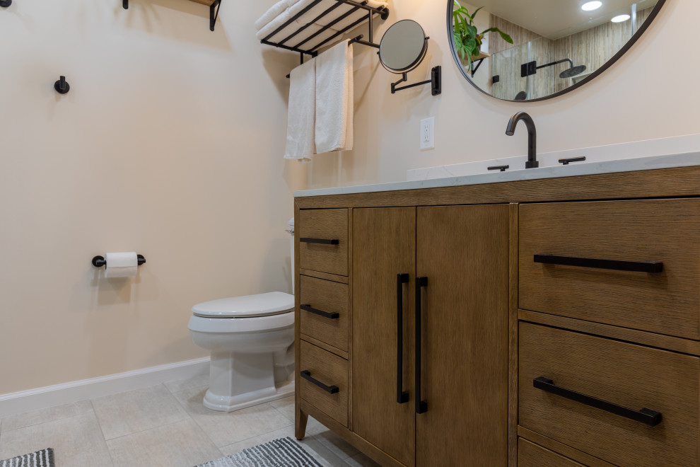 Modern inredning av ett mellanstort vit vitt badrum med dusch, med bruna skåp, en dusch i en alkov, en toalettstol med hel cisternkåpa, keramikplattor, klinkergolv i keramik, ett undermonterad handfat, bänkskiva i kvarts, dusch med gångjärnsdörr, flerfärgad kakel, vita väggar, släta luckor och beiget golv