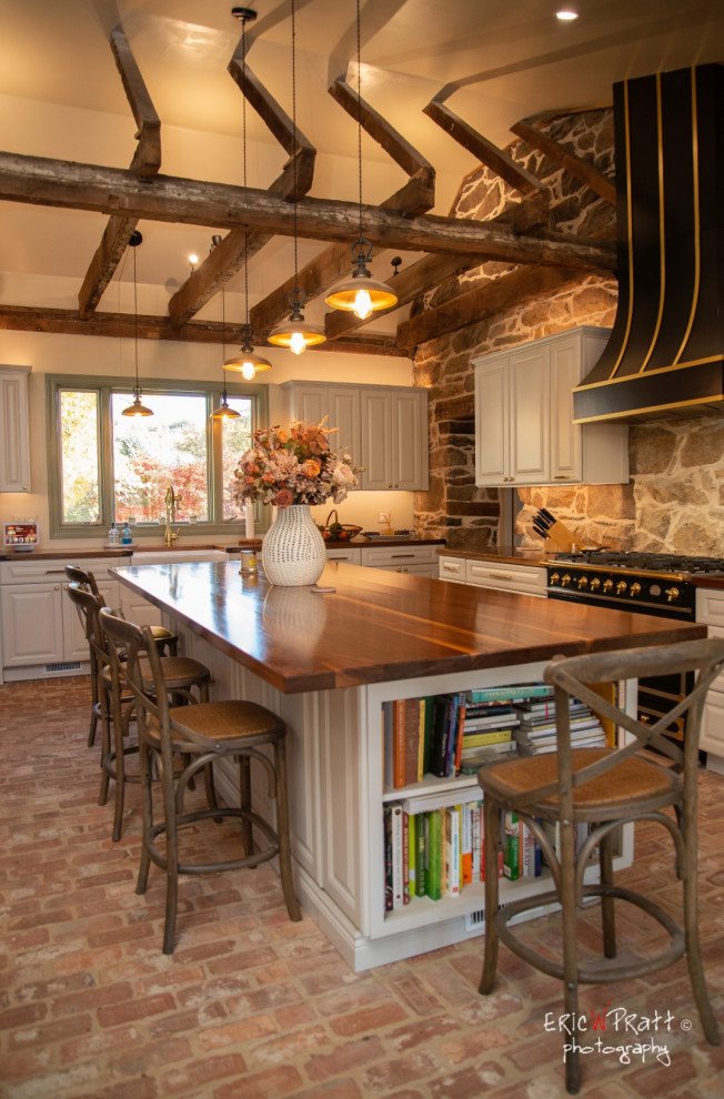 ワシントンD.C.にある高級な広いラスティックスタイルのおしゃれなキッチン (エプロンフロントシンク、レイズドパネル扉のキャビネット、白いキャビネット、木材カウンター、レンガの床、表し梁) の写真