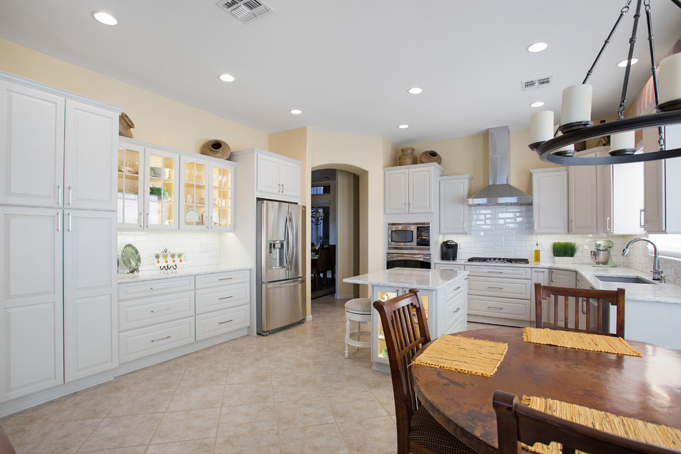 Inspiration for a mid-sized transitional single-wall ceramic tile and beige floor eat-in kitchen remodel with an undermount sink, raised-panel cabinets, white cabinets, quartz countertops, white backsplash, porcelain backsplash, stainless steel appliances and an island