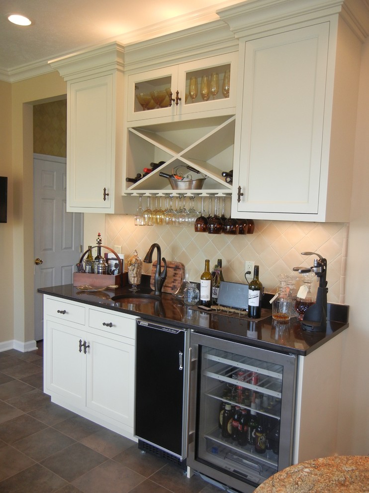 Mid-sized transitional single-wall porcelain tile and brown floor wet bar photo with shaker cabinets, white cabinets, granite countertops, beige backsplash, ceramic backsplash, an undermount sink and black countertops