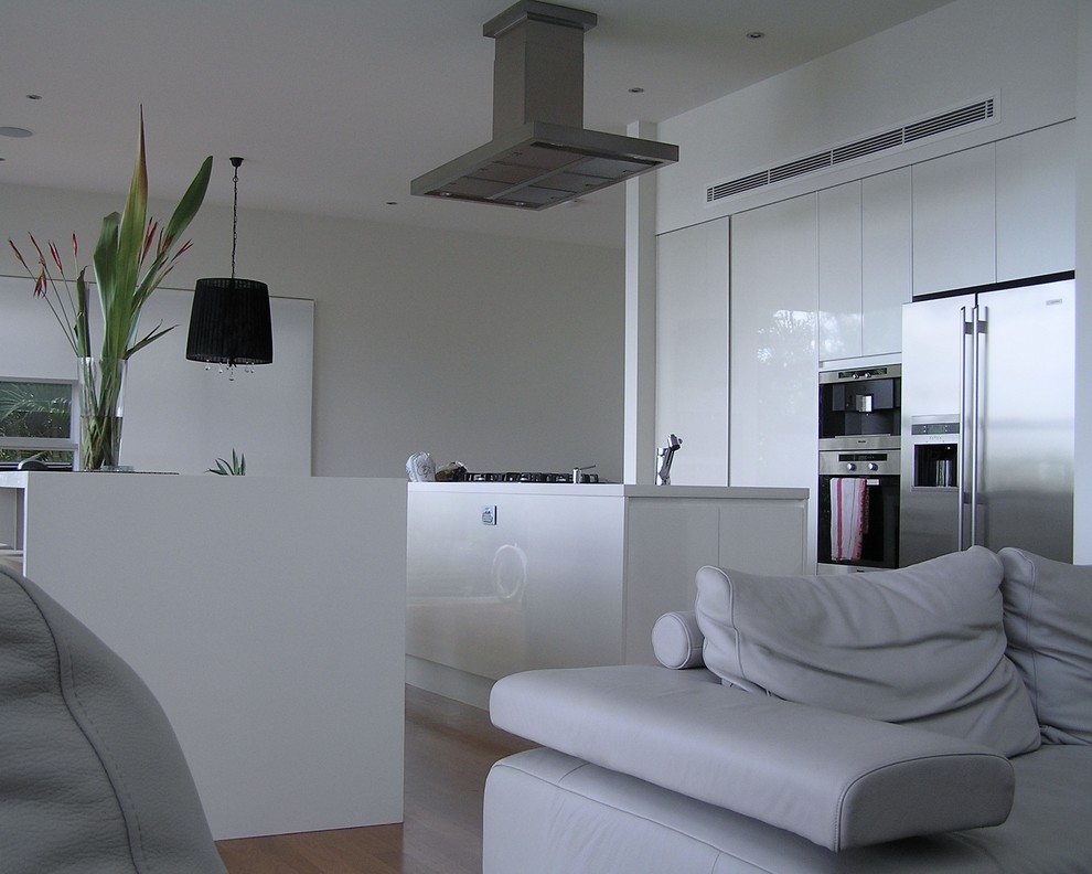 This is an example of a contemporary eat-in kitchen in Brisbane with an undermount sink, flat-panel cabinets, white cabinets, quartz benchtops and stainless steel appliances.