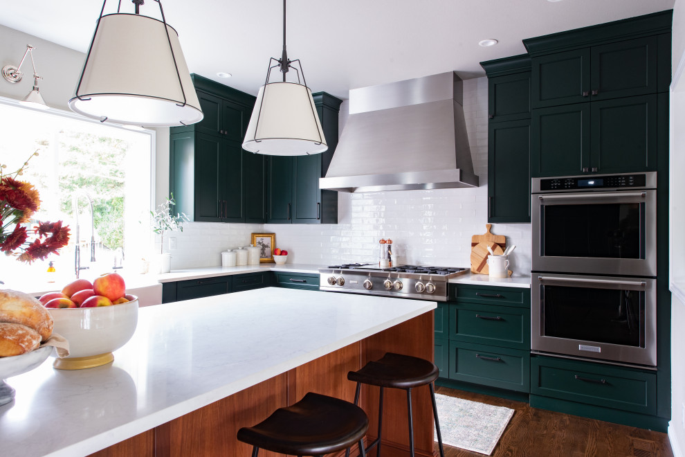 Inspiration for a medium sized traditional l-shaped kitchen/diner in Seattle with a belfast sink, shaker cabinets, green cabinets, white splashback, metro tiled splashback, integrated appliances, dark hardwood flooring, an island, brown floors, green worktops and engineered stone countertops.