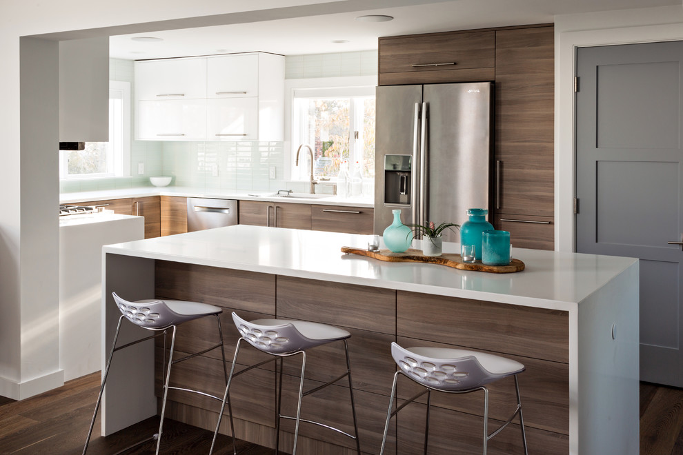 Photo of a beach style u-shaped kitchen in Boston with an undermount sink, flat-panel cabinets, dark wood cabinets, glass tile splashback, stainless steel appliances, dark hardwood floors, with island, brown floor and white benchtop.