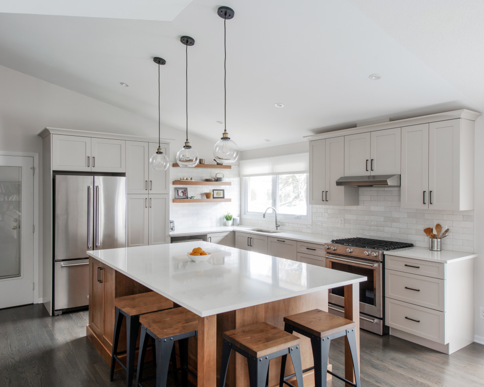 Inspiration for a mid-sized transitional l-shaped medium tone wood floor, gray floor and vaulted ceiling open concept kitchen remodel in Ottawa with a double-bowl sink, shaker cabinets, gray cabinets, quartz countertops, white backsplash, subway tile backsplash, stainless steel appliances, an island and white countertops
