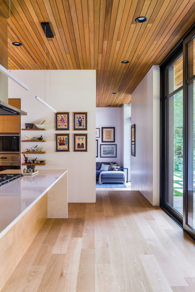 Contemporary l-shaped open plan kitchen in Portland with flat-panel cabinets, light wood cabinets, quartz benchtops, stainless steel appliances, light hardwood floors, with island, white benchtop and wood.