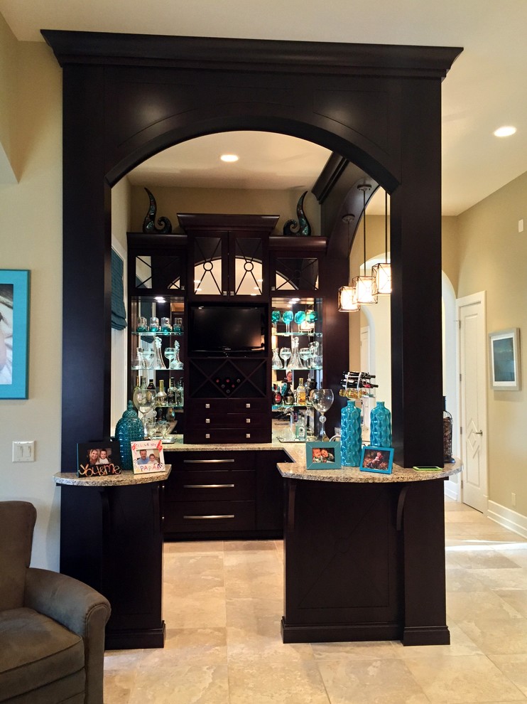 Photo of a large traditional u-shaped wet bar in Other with flat-panel cabinets, black cabinets, granite benchtops, travertine floors, beige floor and an undermount sink.