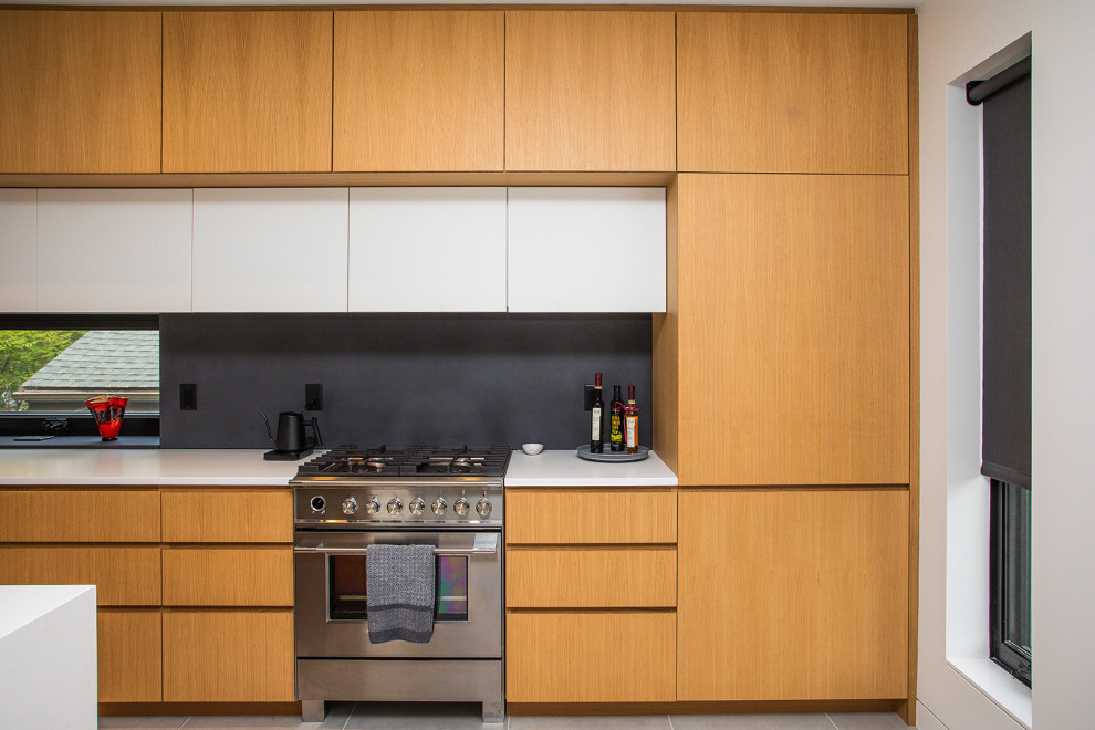 This is an example of a mid-sized modern single-wall eat-in kitchen in Portland with flat-panel cabinets, light wood cabinets, stone slab splashback, cement tiles, white benchtop, a drop-in sink, black splashback, with island and grey floor.