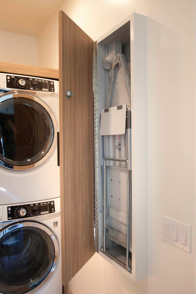 Photo of a small beach style l-shaped dedicated laundry room in San Diego with an undermount sink, flat-panel cabinets, light wood cabinets, quartz benchtops, blue splashback, cement tile splashback, white walls, porcelain floors, a stacked washer and dryer, beige floor and white benchtop.