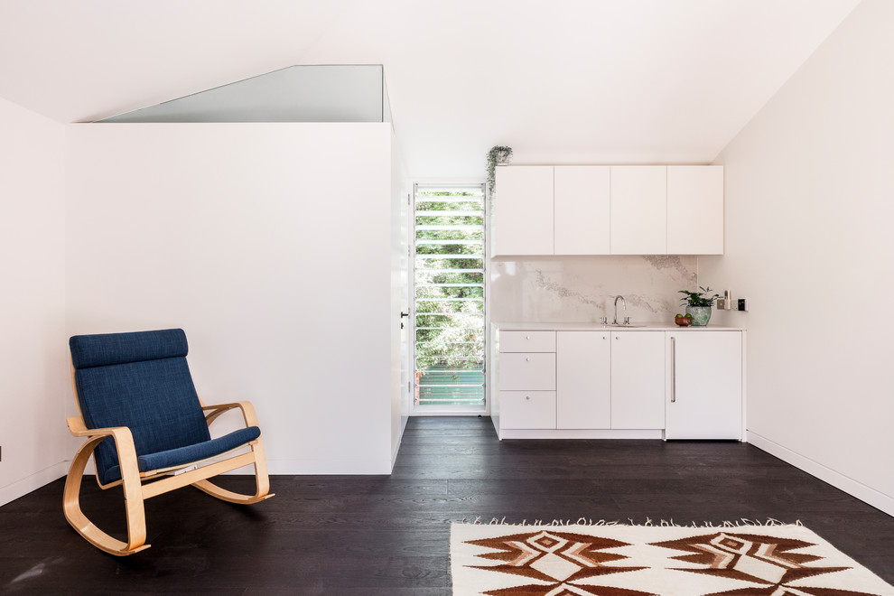 This is an example of a contemporary single-wall wet bar in Sydney with flat-panel cabinets, white cabinets, beige splashback, dark hardwood floors, brown floor and white benchtop.