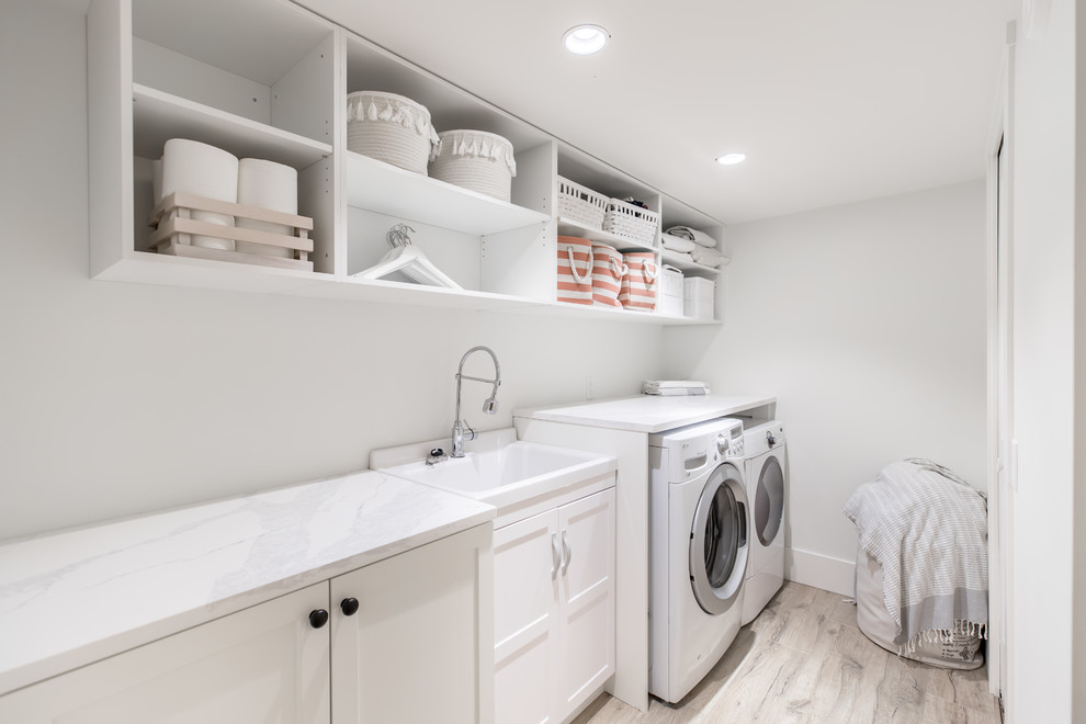 Mid-sized arts and crafts single-wall dedicated laundry room in Vancouver with an utility sink, recessed-panel cabinets, white cabinets, quartzite benchtops, white walls, porcelain floors, a side-by-side washer and dryer, grey floor and white benchtop.