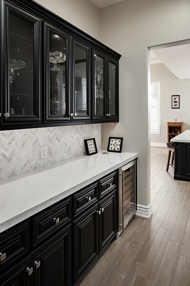 Open concept kitchen - large transitional l-shaped light wood floor and brown floor open concept kitchen idea in Phoenix with an undermount sink, raised-panel cabinets, black cabinets, quartz countertops, white backsplash, marble backsplash, stainless steel appliances and an island