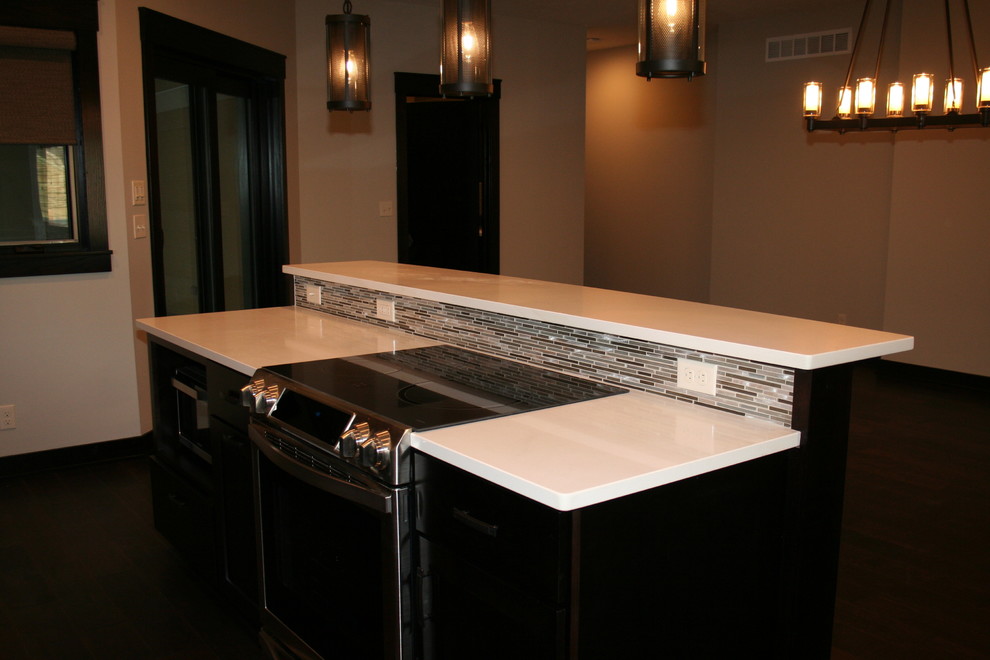 Open concept kitchen - mid-sized transitional l-shaped dark wood floor and brown floor open concept kitchen idea with stainless steel appliances, an island, an undermount sink, shaker cabinets, black cabinets, quartz countertops, beige backsplash and porcelain backsplash