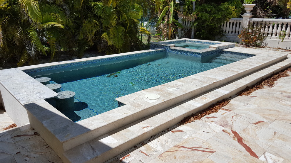 Inspiration for a mid-sized tropical backyard rectangular natural pool in Miami with a hot tub and natural stone pavers.