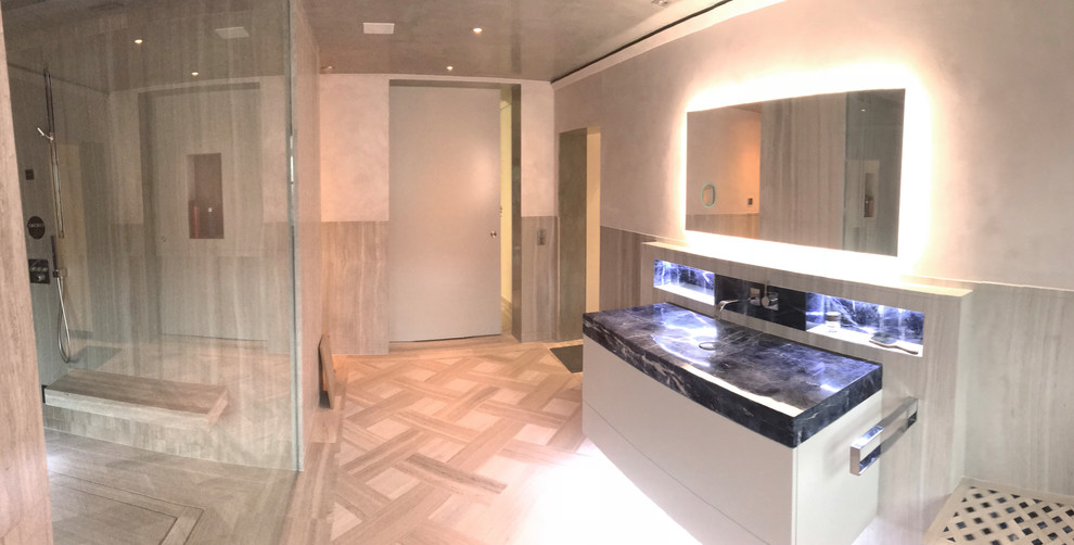 This is an example of a large contemporary master bathroom in Dusseldorf with flat-panel cabinets, grey cabinets, a curbless shower, a two-piece toilet, gray tile, stone slab, grey walls, an integrated sink, grey floor, an open shower and blue benchtops.