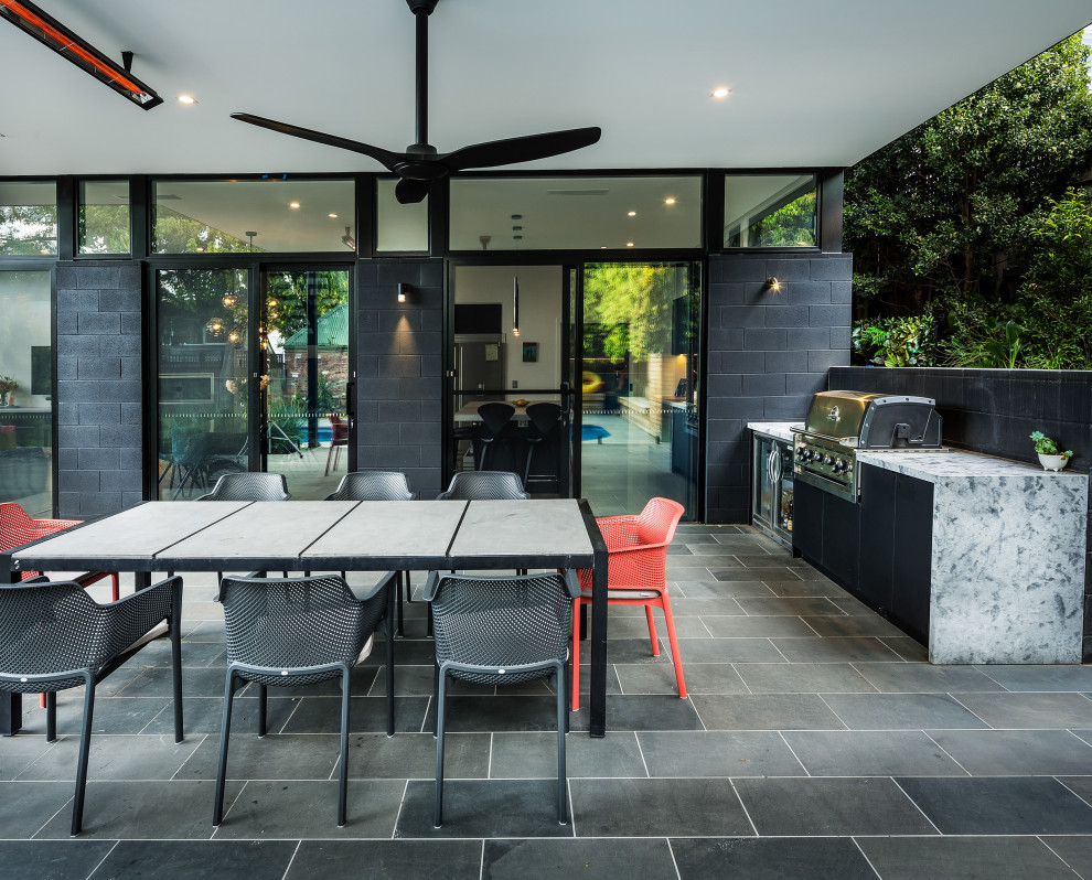 Large contemporary backyard patio in Melbourne with an outdoor kitchen, natural stone pavers and an awning.