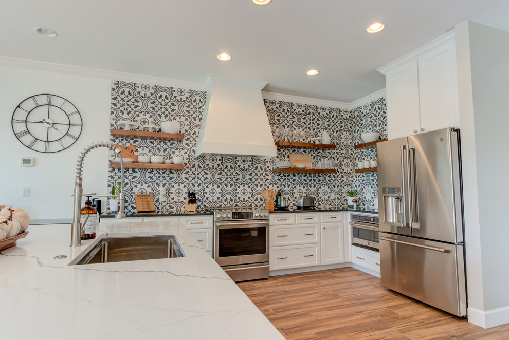 Example of a large transitional l-shaped ceramic tile and brown floor eat-in kitchen design with an undermount sink, shaker cabinets, white cabinets, quartz countertops, multicolored backsplash, ceramic backsplash, stainless steel appliances, an island and white countertops