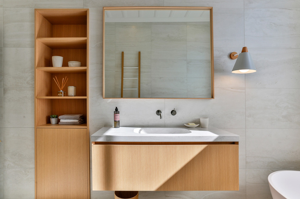 Inspiration for a mid-sized traditional 3/4 bathroom in Auckland with furniture-like cabinets, light wood cabinets, a freestanding tub, an alcove shower, a one-piece toilet, gray tile, ceramic tile, grey walls, ceramic floors, a console sink, marble benchtops, grey floor, a hinged shower door and white benchtops.