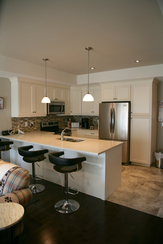 Example of a small transitional u-shaped porcelain tile eat-in kitchen design in Toronto with an undermount sink, flat-panel cabinets, white cabinets, solid surface countertops, beige backsplash, glass tile backsplash, stainless steel appliances and an island