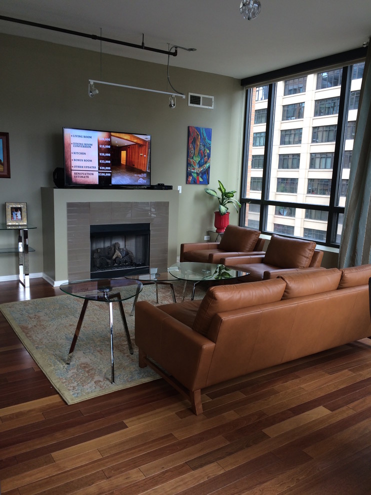 Mid-sized modern loft-style living room in Chicago with green walls, medium hardwood floors, a standard fireplace, a tile fireplace surround, a wall-mounted tv and brown floor.