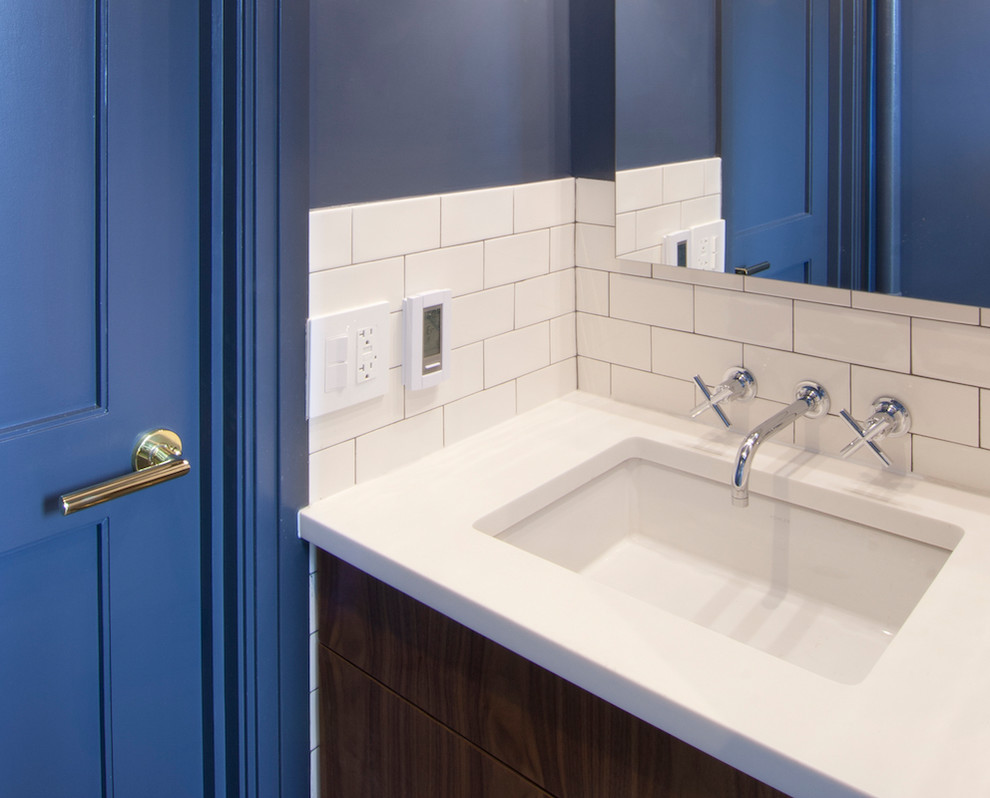 This is an example of a small transitional bathroom in New York with flat-panel cabinets, medium wood cabinets, an alcove tub, a shower/bathtub combo, a one-piece toilet, white tile, ceramic tile, blue walls, terra-cotta floors, an undermount sink, engineered quartz benchtops, blue floor, a shower curtain and white benchtops.
