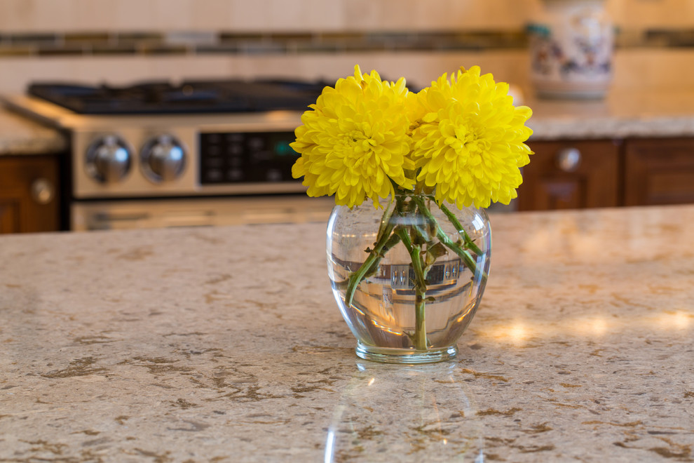 Large transitional l-shaped medium tone wood floor and brown floor eat-in kitchen photo in Denver with a farmhouse sink, raised-panel cabinets, medium tone wood cabinets, granite countertops, beige backsplash, stone tile backsplash, stainless steel appliances and an island