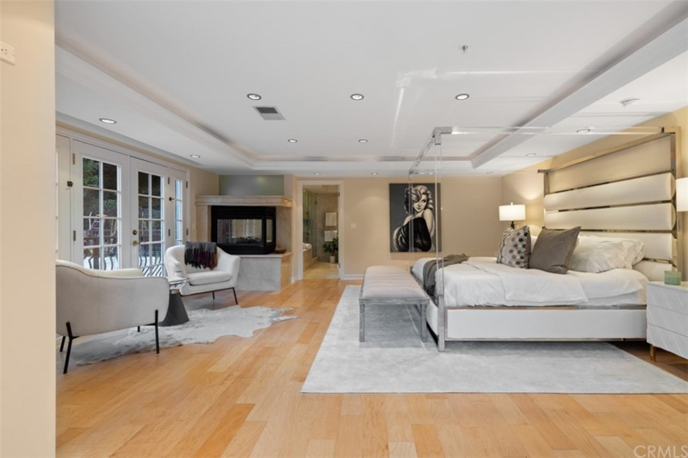 Großes Modernes Hauptschlafzimmer mit beiger Wandfarbe, Eckkamin, gefliester Kaminumrandung, braunem Boden, eingelassener Decke und hellem Holzboden in Los Angeles