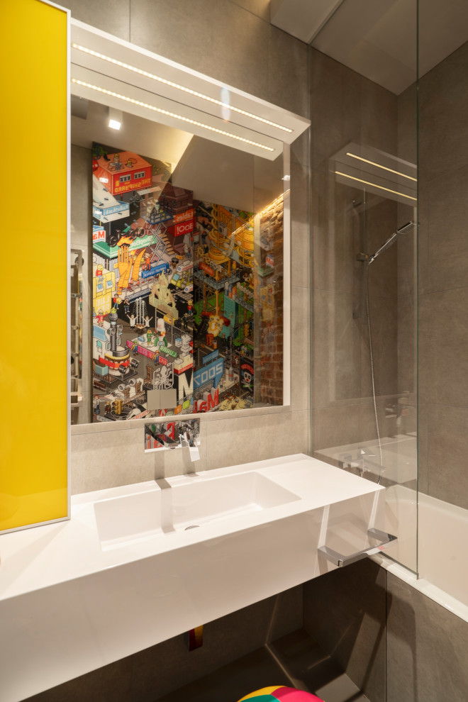 Bild på ett litet industriellt vit vitt badrum för barn, med släta luckor, gula skåp, våtrum, en vägghängd toalettstol, grå kakel, porslinskakel, betonggolv, ett integrerad handfat, bänkskiva i akrylsten, grått golv och dusch med skjutdörr
