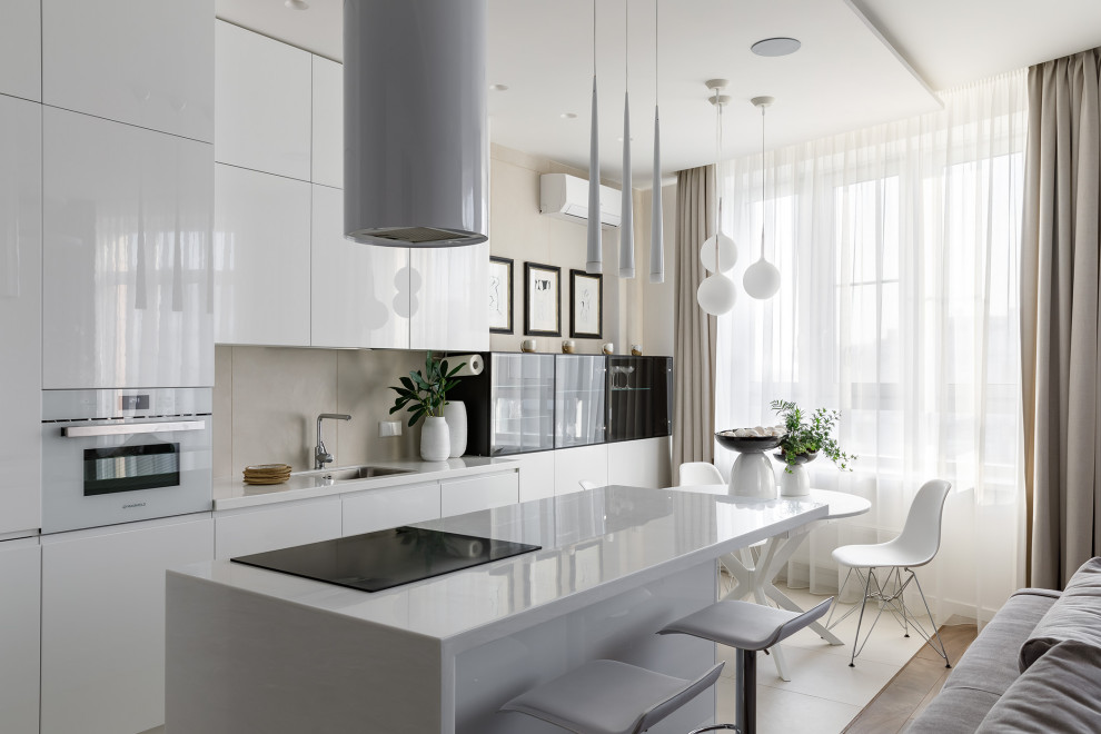 Идея дизайна: параллельная, светлая кухня-гостиная в современном стиле с врезной мойкой, плоскими фасадами, белыми фасадами, бежевым фартуком, белой техникой, островом, белым полом и белой столешницей