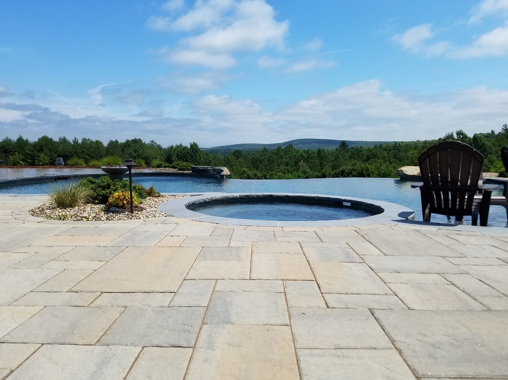 Inspiration for an expansive country backyard custom-shaped infinity pool in Boston with a pool house and concrete pavers.