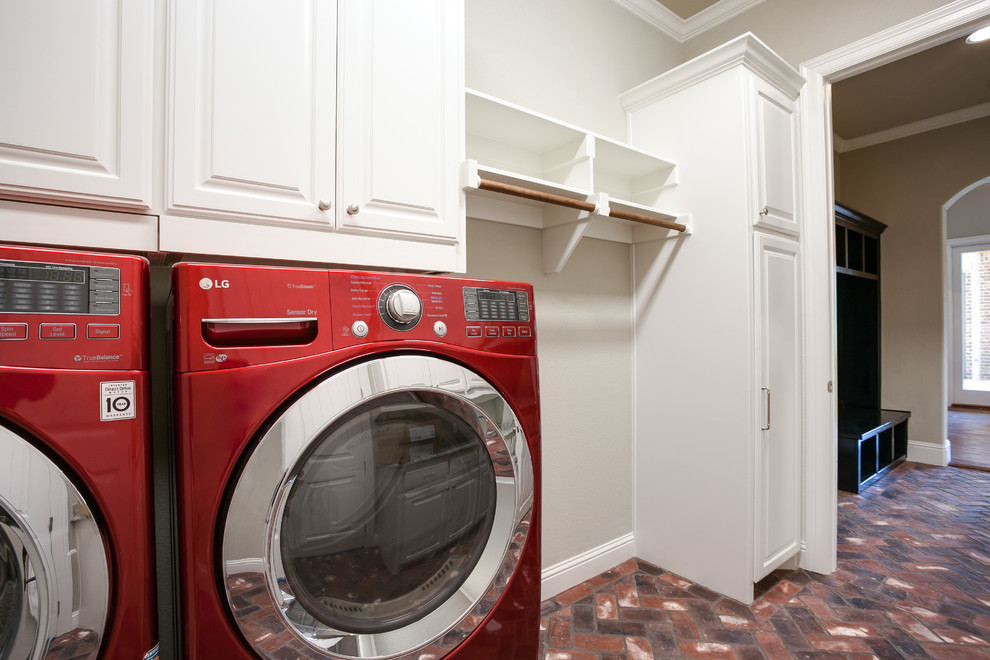 Large country galley utility room in Dallas with raised-panel cabinets, white cabinets, beige walls, brick floors and a side-by-side washer and dryer.