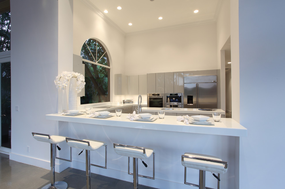 Photo of a large modern u-shaped separate kitchen in Miami with a single-bowl sink, flat-panel cabinets, white cabinets, solid surface benchtops, stainless steel appliances, concrete floors and with island.